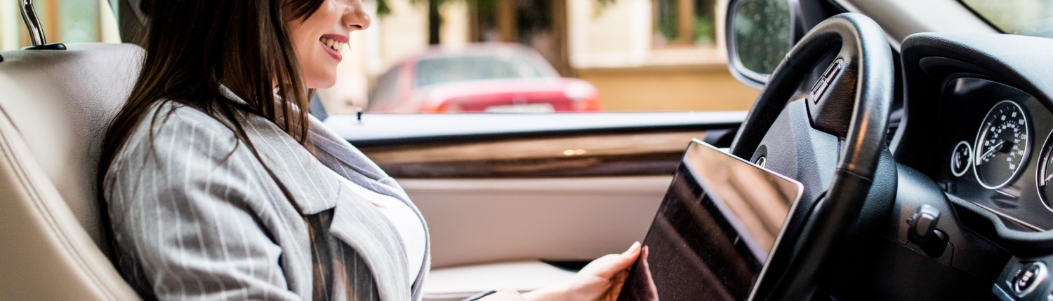Beautiful young business woman using laptop and phone in the car.
