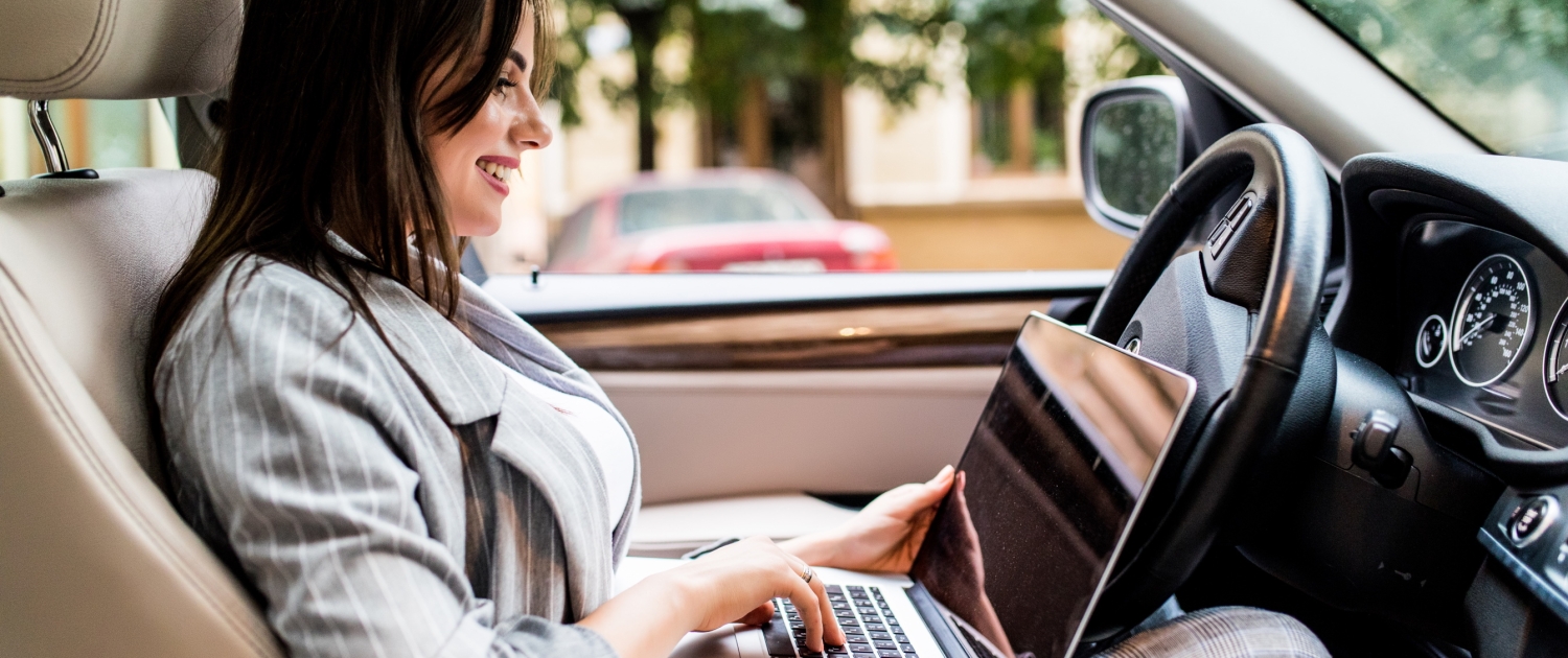 Beautiful young business woman using laptop and phone in the car.